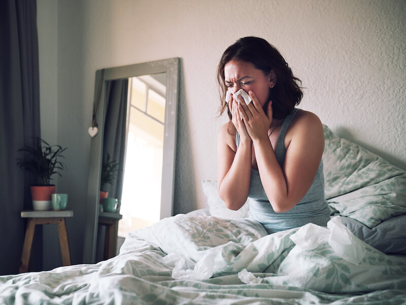 Woman in bed sneezing with allergies that are clogging her ear.