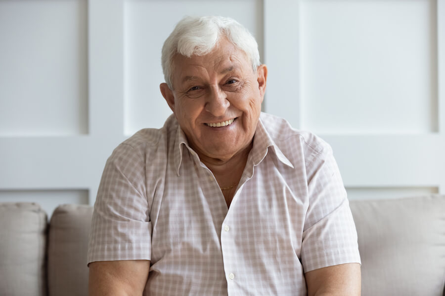 Mature man smiling on couch because now he can hear the TV with his hearing aids.