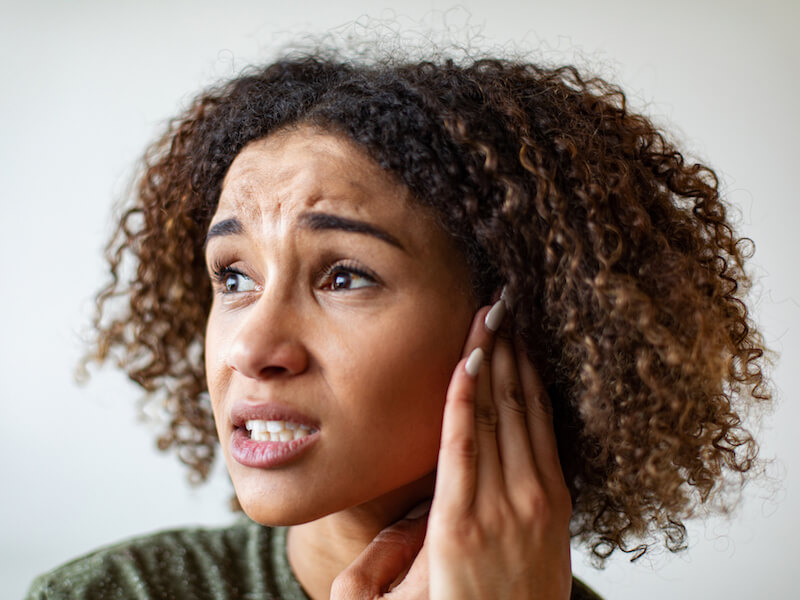 Woman with hearing loss touching her ear and thinking about preventing further loss.