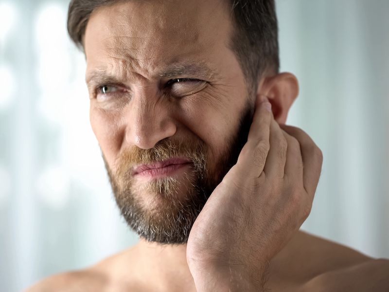 Man touching ear in response to crackling noises in his ear.