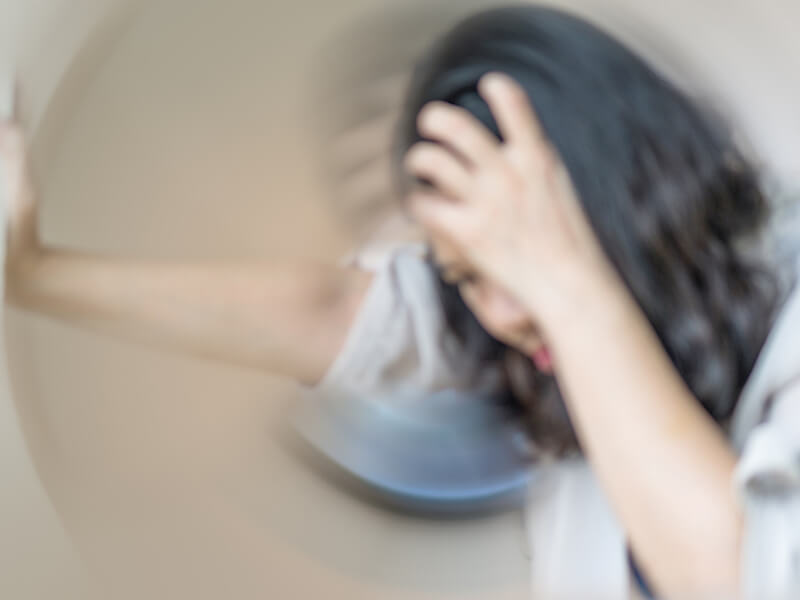 Woman leaning against wall because of recurring dizziness.