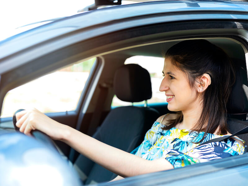 Woman with dark hair wearing a hearing aid happily driver her car