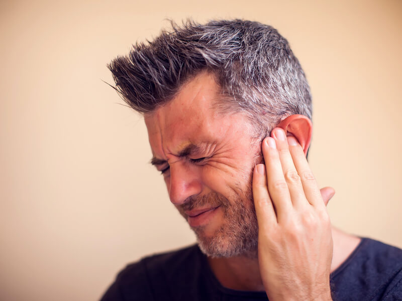 Man plugging ear with index finger because he suffers from tinnitus