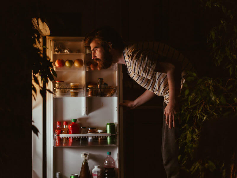 Man looking for snacks in the refrigerator late night.
