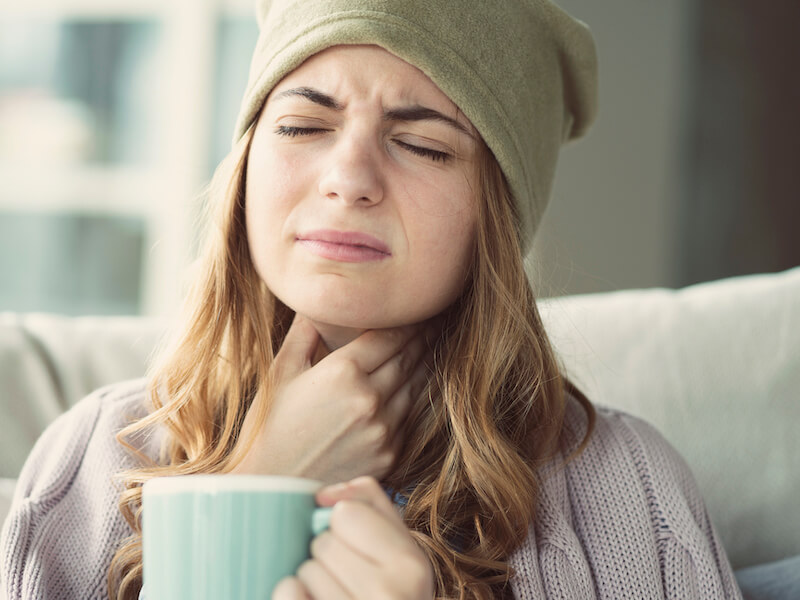 Young woman suffering from cold and sore tonsils drinking tea to lesson symptoms.