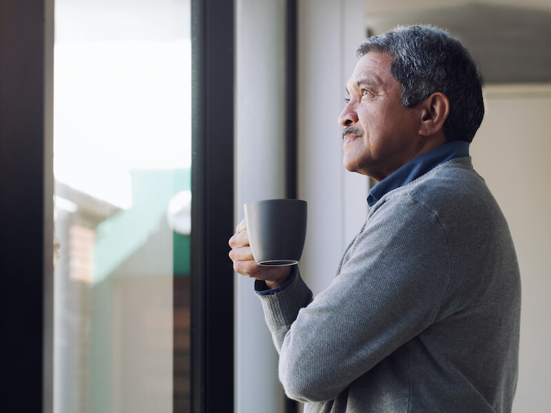 Shot of a senior man drinking coffee and looking thoughtfully out of a window wondering about hearing loss.