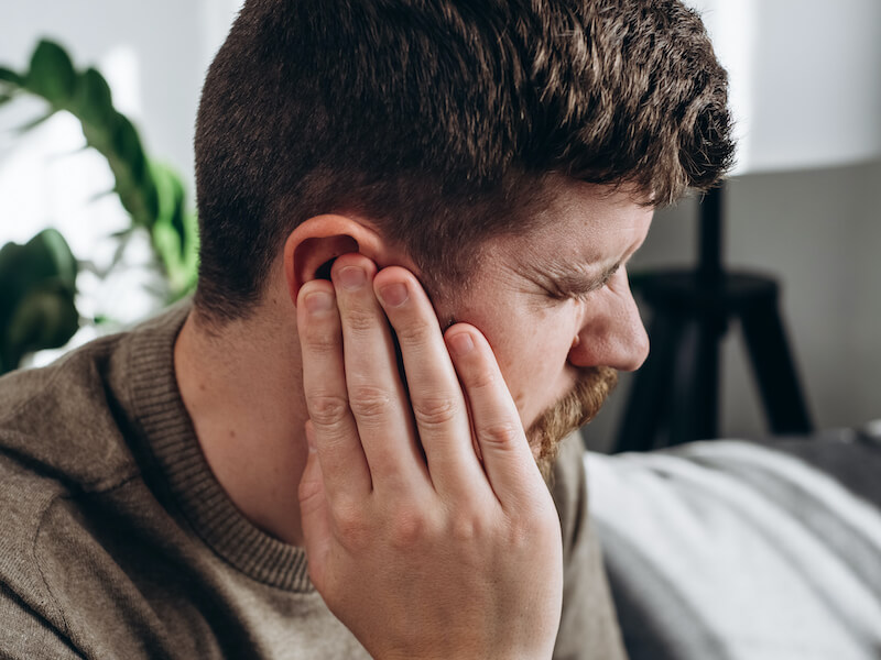 Man suffering from sudden hearing loss sitting on the couch touching his ear.