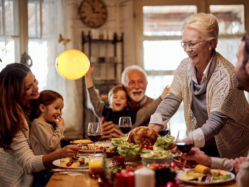 Happy mature woman who no longer suffers from hearing loss, serving food to her family during Thanksgiving meal at dining table.