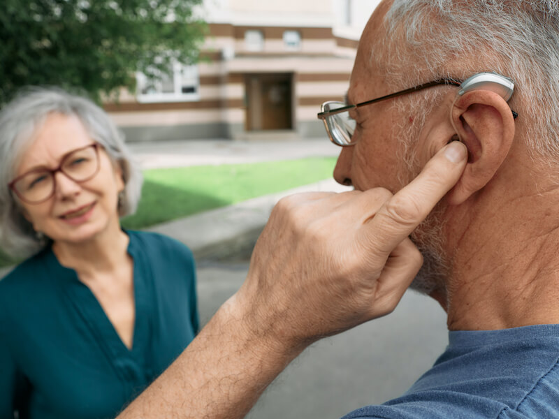 Man having troubles with his hearing aids while trying to communicate with his friend.