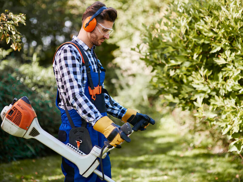 Man with weedwacker wearing hearing protection cutting the grass