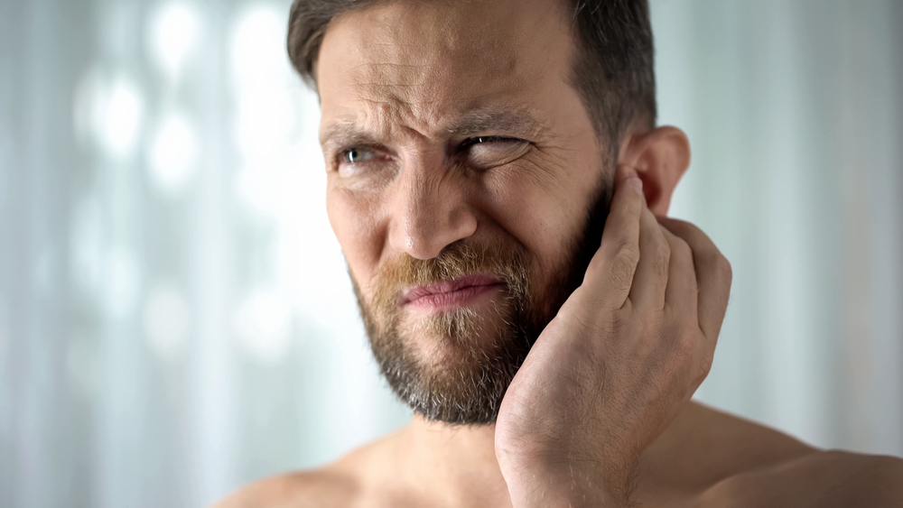 man with hand over itchy ear.